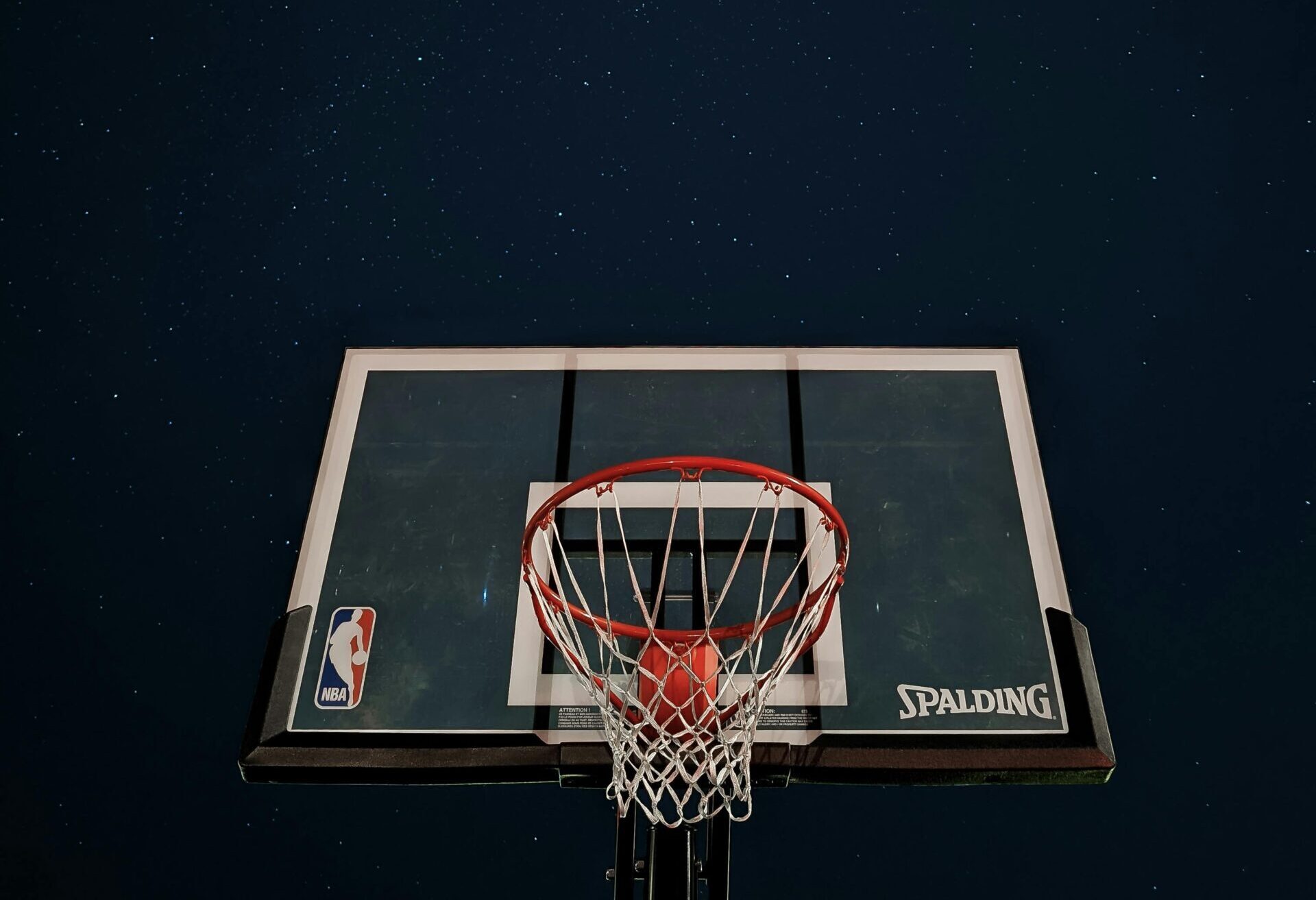 A basketball hoop silhouetted against a dark night sky filled with stars.