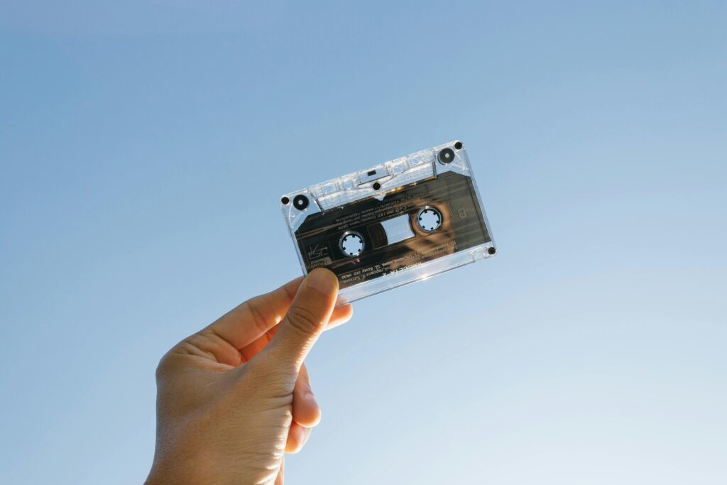 A person holds a vintage cassette tape against a clear blue sky, symbolizing nostalgia and technology.